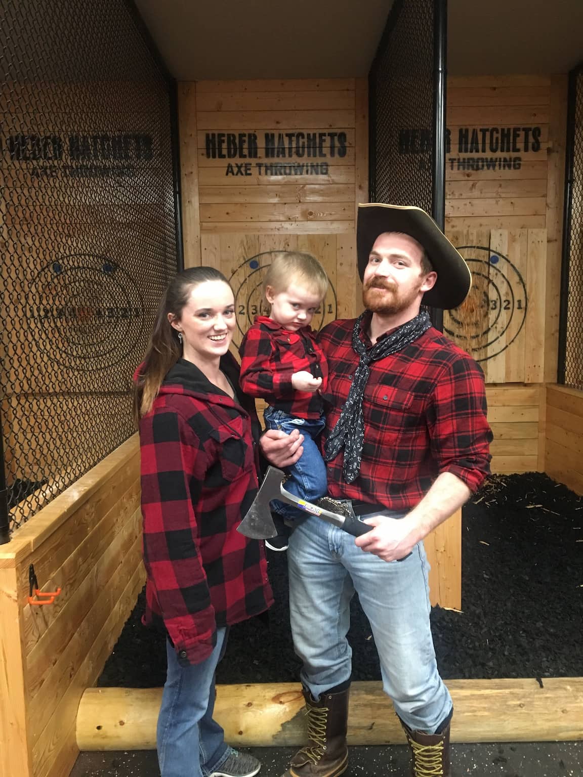 A family wearing flannel poses with an axe at Heber Hatchets in Rexburg